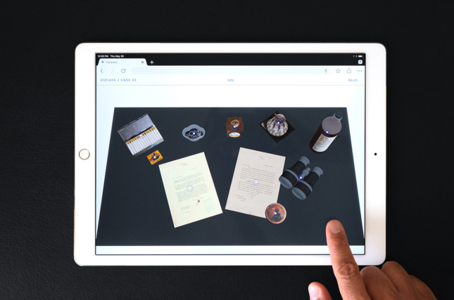 An iPad displays an array of items—letters, cigarette case, binoculars, etc.