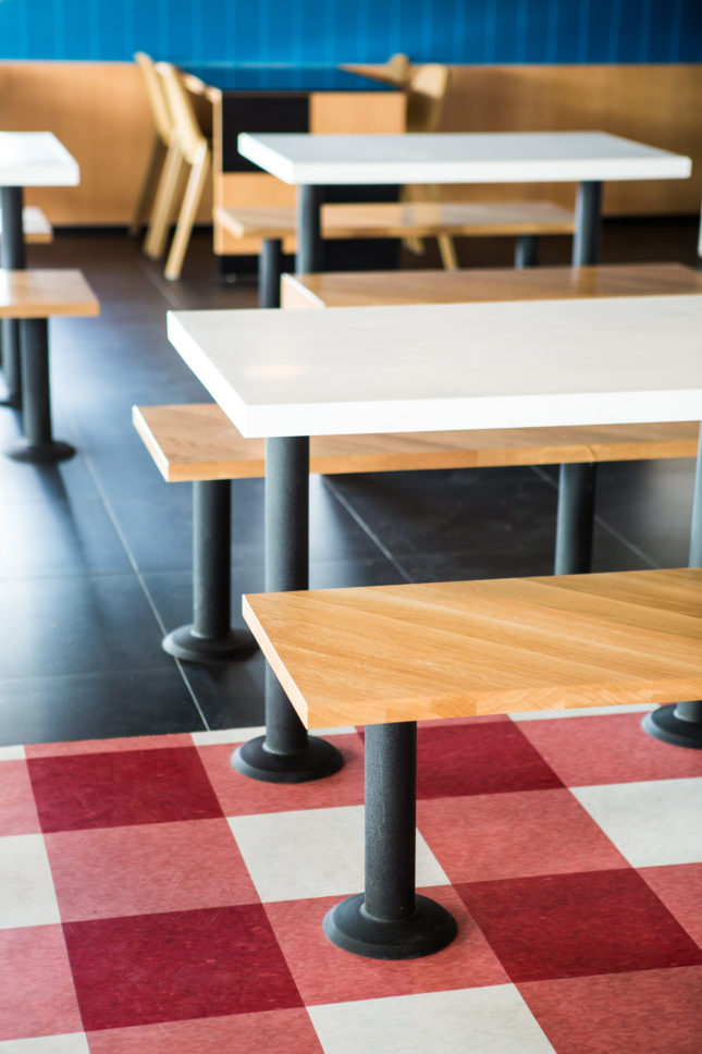 Johnson and Rudolph’s large scale gingham patterned VCT floor tiles mark the kitchen pass while bifurcated table tops allow for flexible use of the space’s large tables. (Courtesy Laure Joliet)