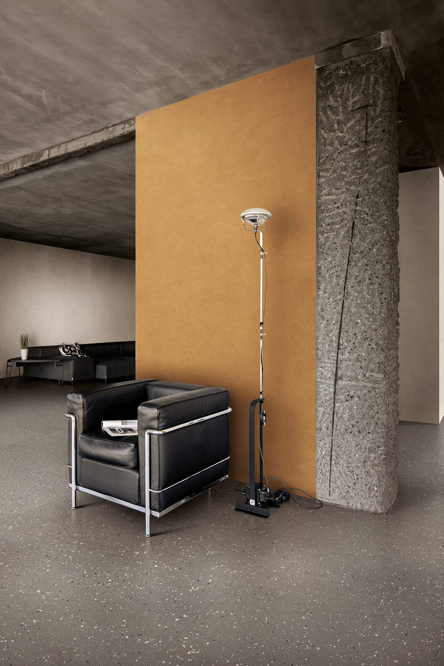 A 1950's black leather chair in front of a concrete column and camel, terrazzo-like speckled wall