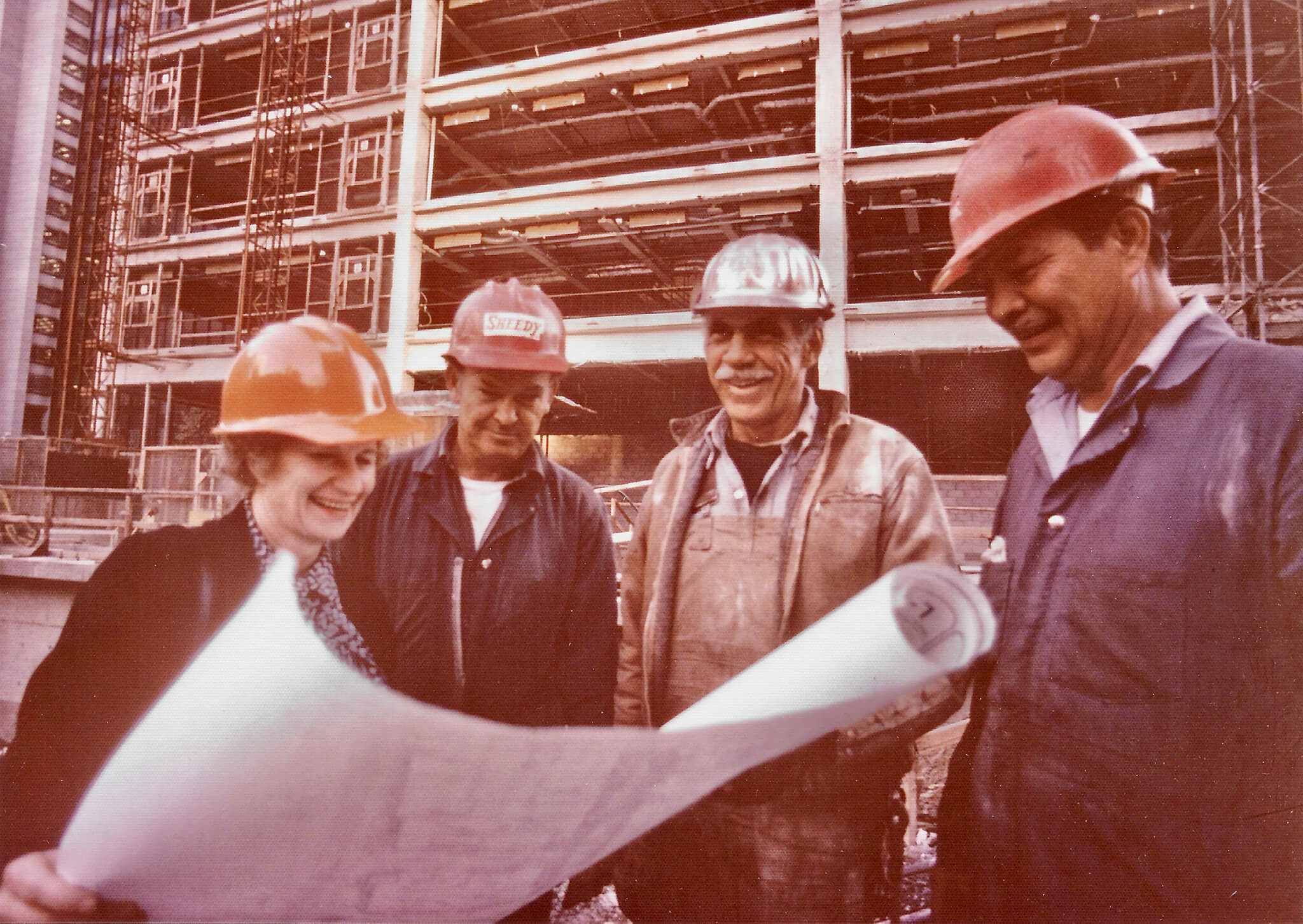 Beverly Willis in a hard hat on a construction site with three construction workers and a building in the background