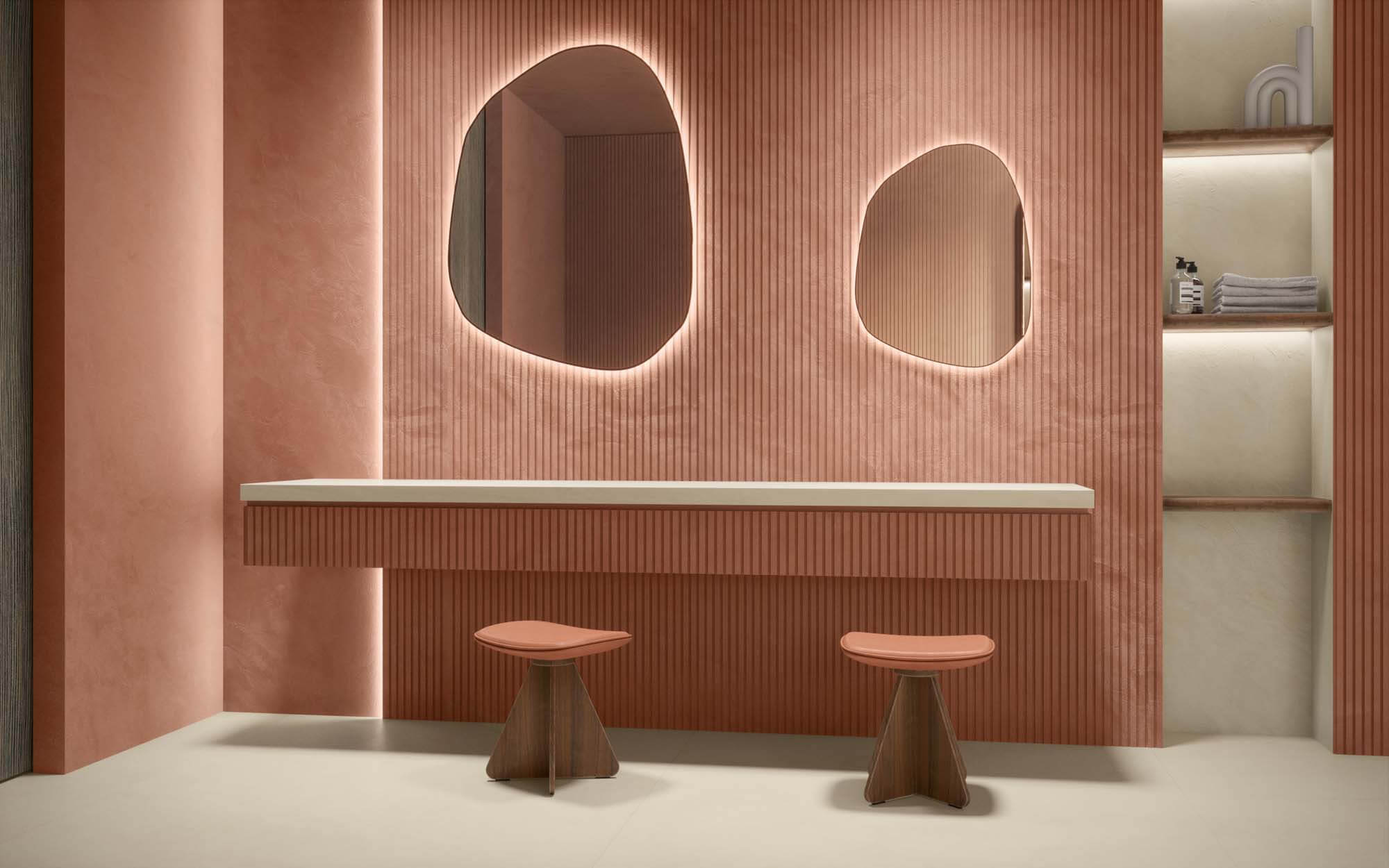 Unique vanity with curved mirrows in front of warm pink vertical tiles