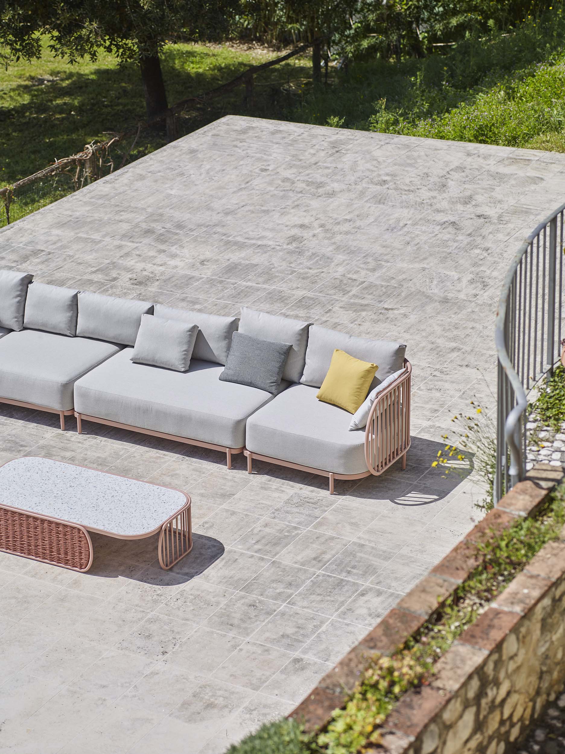 Light grey cushioned outdoor furniture sofa with pink metal sides.