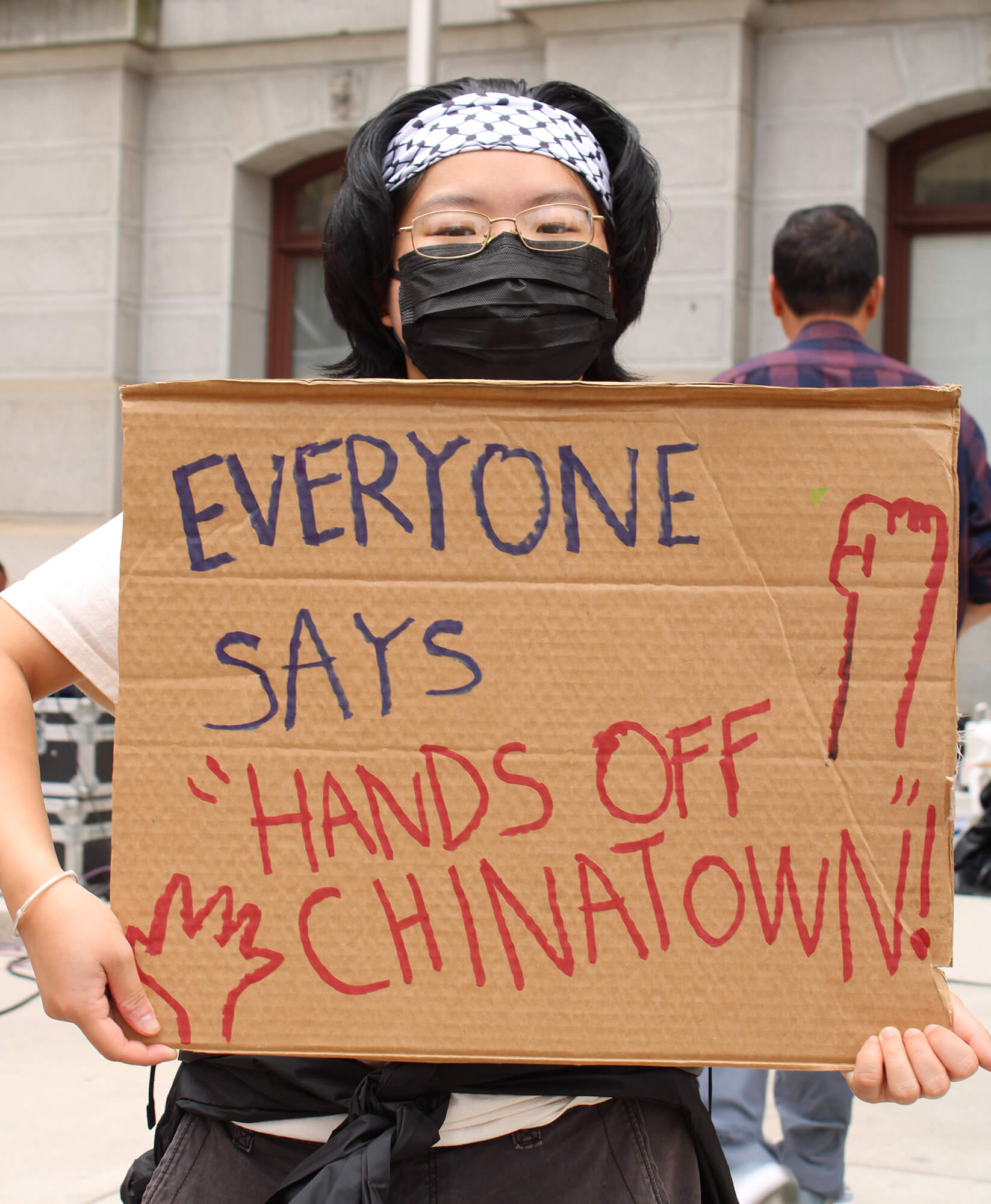 a protestor holds a sign that reads Everyone Says Hands Off Chinatown