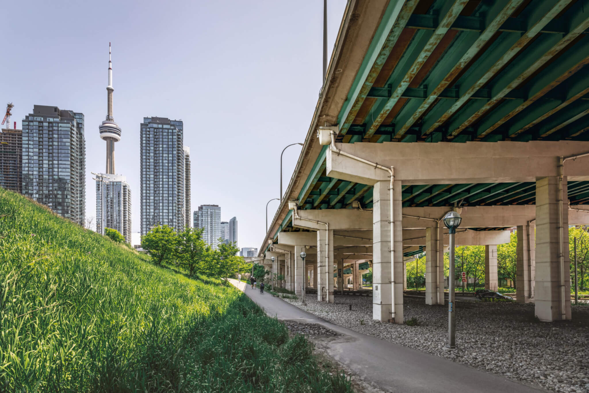 part of the Bentway under bridge next to grass with city in background